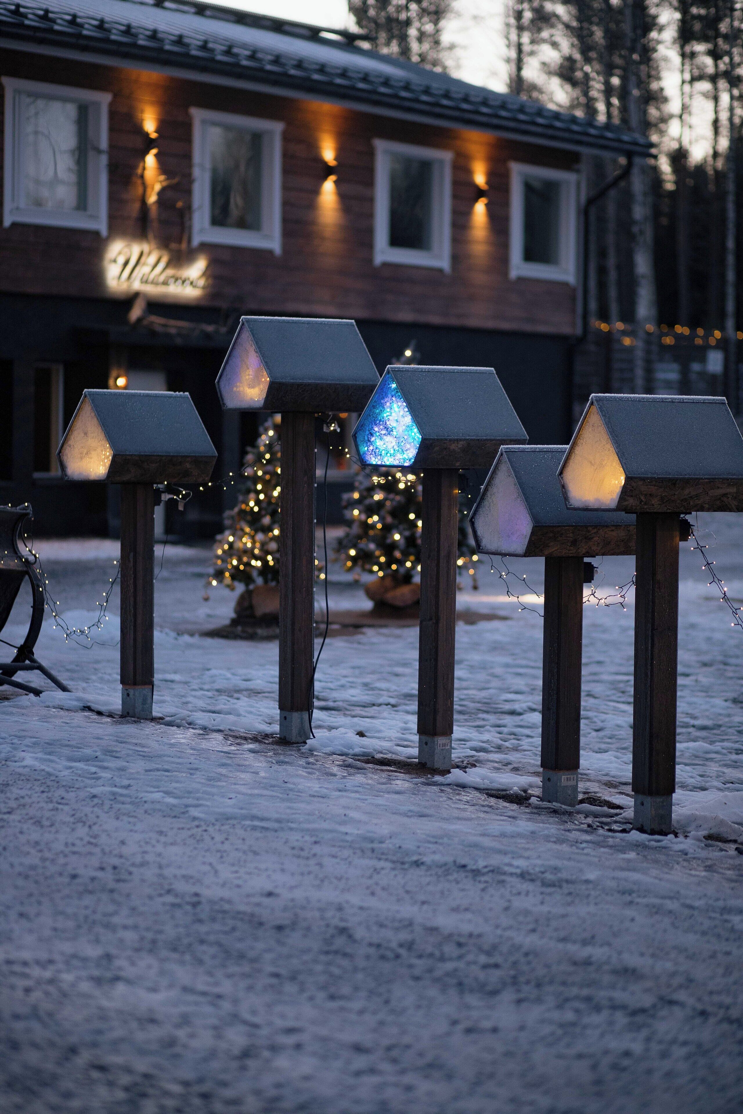 Un edificio con un letrero que dice 'Welcome', suelo cubierto de nieve y faroles hexagonales iluminados.