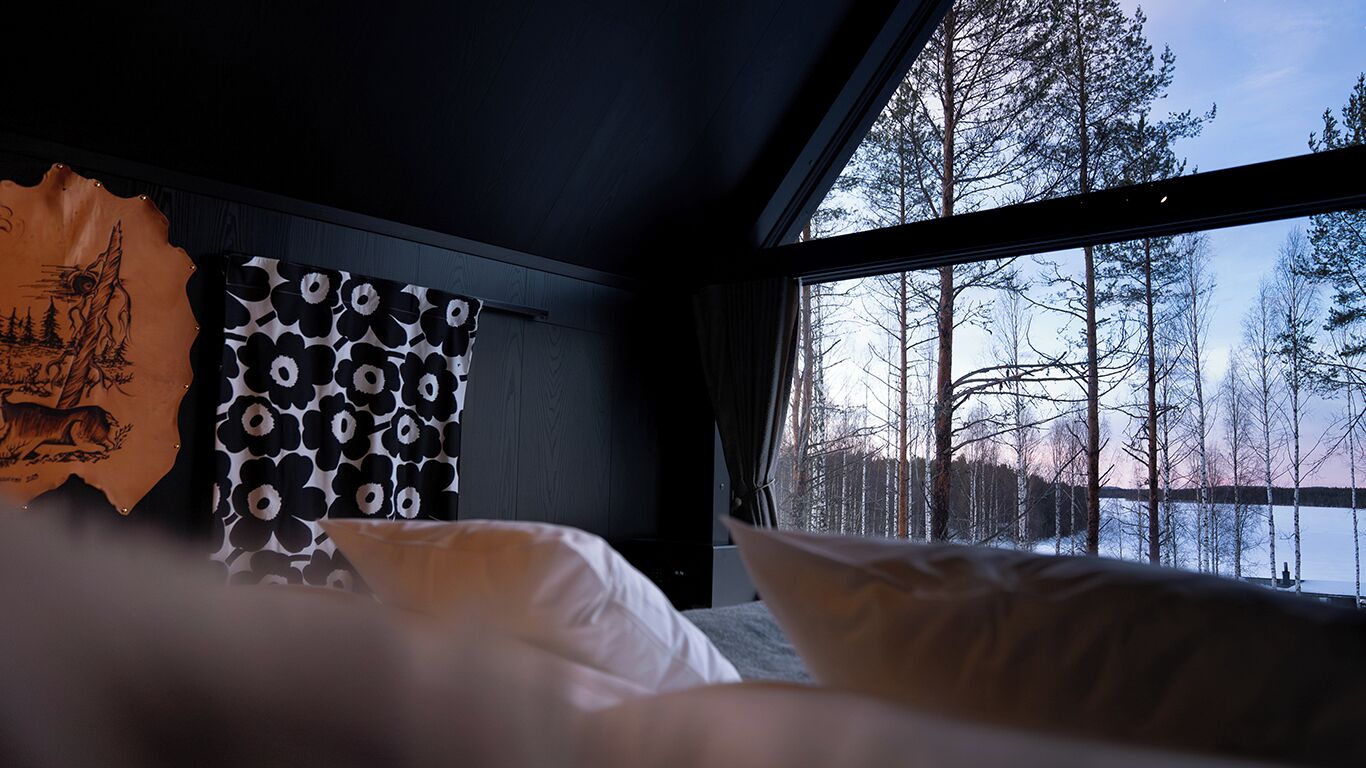 A bedroom with a large window, a bed, and a wall with a patterned curtain.
