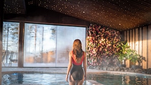 A woman in a swimsuit standing in a hot tub with a large window and floral wall in the background. - Aito  Igloo & Spa Resort (Rovaniemi)