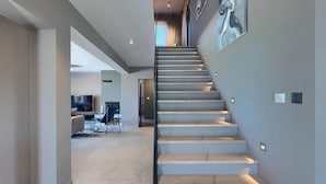 Una escalera moderna con diseño minimalista que conduce a una sala de estar con televisor y asientos.