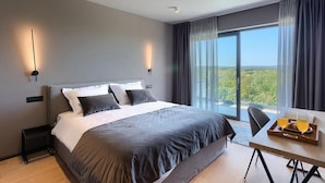 Habitación de hotel moderna con una cama grande, una mesa de comedor con sillas y vistas al exterior.
