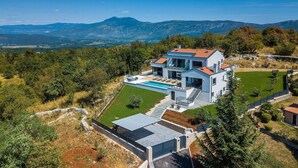 Una casa moderna de dos pisos con piscina, rodeada de césped cuidado y árboles.