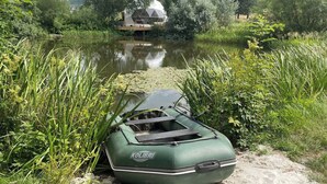A green inflatable boat with the brand "KOLIBRI" on a riverbank with dense vegetation and a house in the background. - Lake View Dome Sleeps 6 -hot tub -fireplace (Horni Podluzi)