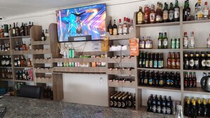 A bar area with shelves stocked with various liquor bottles, a television mounted on the wall, and a countertop with a Coca-Cola bottle. - WHITE HOUSE LOUNGE & GUEST HOUSE (Eldoret)