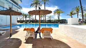 Un espace aménagé au bord de la piscine, avec des chaises longues et des parasols, une piscine à l’eau d’un bleu limpide et des palmiers.