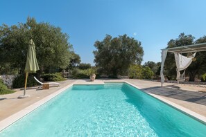 A rectangular swimming pool with clear blue water, surrounded by a stone wall and lush greenery.