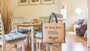 A dining area with a table set for two, a chair with a blue cushion, and a tote bag with text. - Hearts Delight Cottage by Bloom Stays -  a holiday let that sleeps 4 guests  in 2 bedrooms (Canterbury)