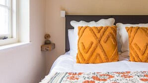A neatly made bed with white linens and two mustard-colored pillows, a small bedside table with a vase, and a framed picture on the wall. - Hearts Delight Cottage by Bloom Stays -  a holiday let that sleeps 4 guests  in 2 bedrooms (Canterbury)