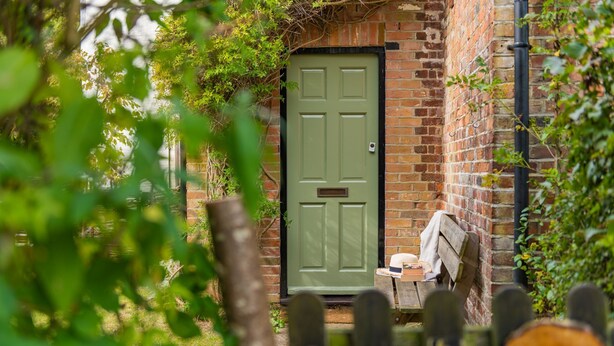 A green door with a mailbox, a brick wall, and a wooden fence with a sign. - Hearts Delight Cottage by Bloom Stays -  a holiday let that sleeps 4 guests  in 2 bedrooms (Canterbury)