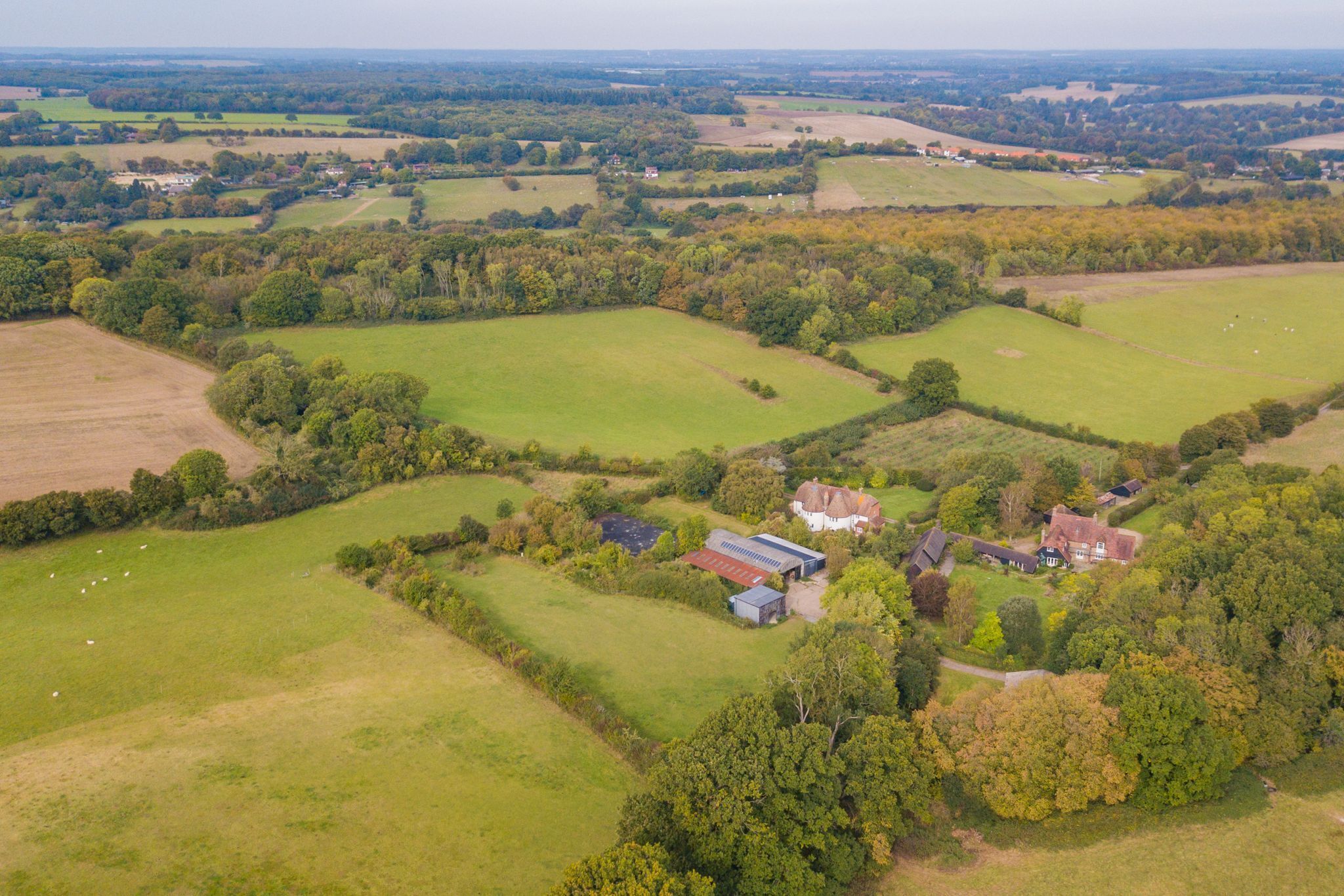An aerial view of a rural property with multiple buildings, green fields, and scattered trees.
