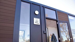 Un bâtiment moderne doté d’une grande porte vitrée, d’une enseigne indiquant qu’il est géré par « Away », et dont l’intérieur est visible, avec un lit et des vêtements.