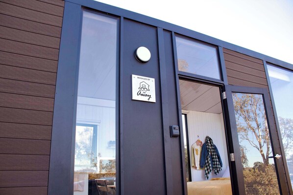 A modern building with a large glass door, a sign indicating management by 'Away,' and a visible interior with a bed and clothing items.