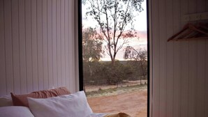 Une chambre à coucher avec un lit, des oreillers et une fenêtre donnant sur des arbres et une clôture.