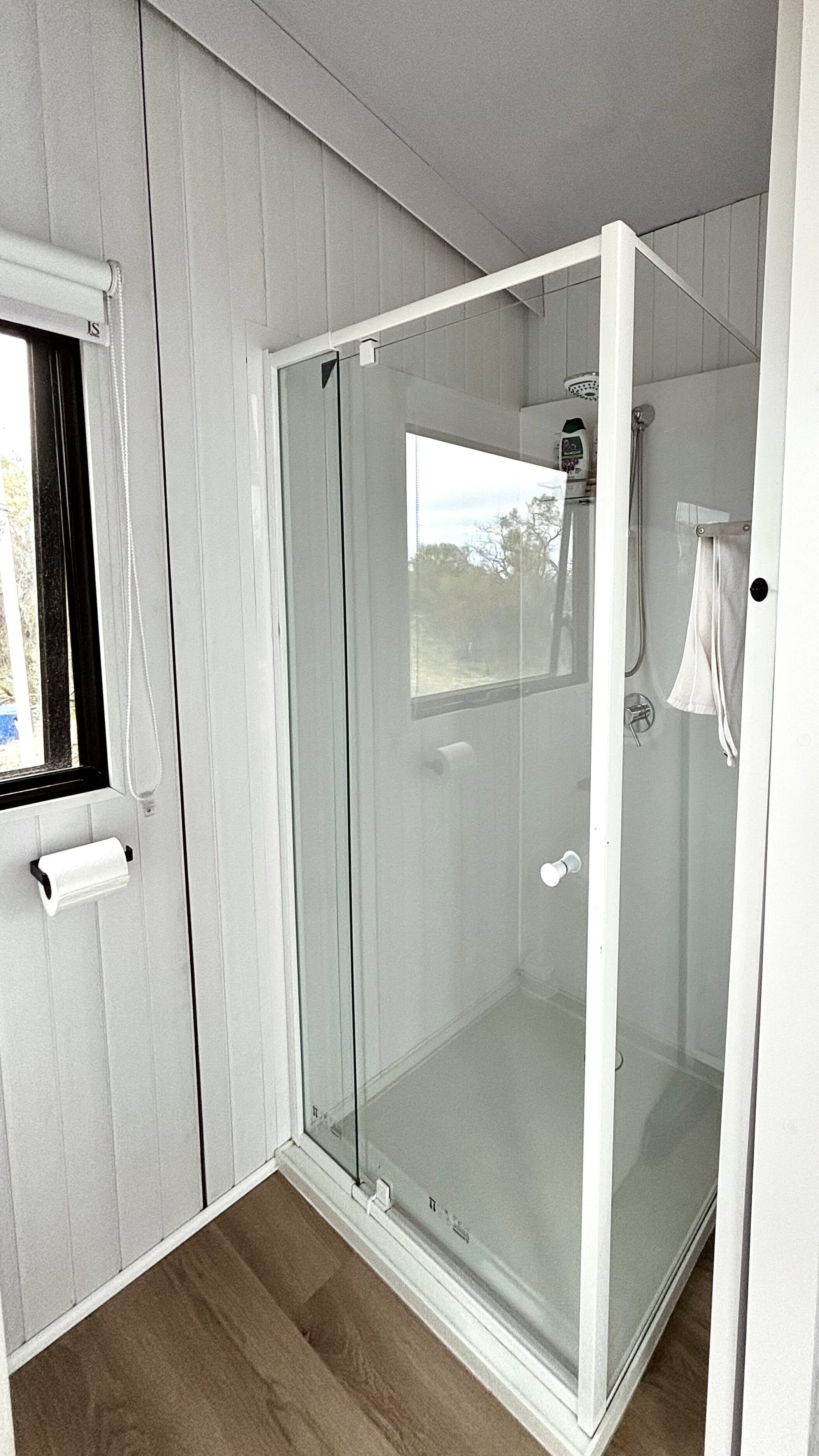 Un baño moderno con cabina de vidrio, ventana y perchero.