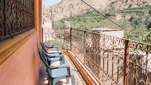 Un balcon orné de balustrades en fer forgé, un luminaire suspendu en osier et une vue sur un paysage montagneux.