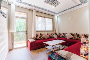 A room with a red sofa, a small table, and a window with a view of greenery. - Les Meilleurs Hébergements à Ourika (Marrakech)