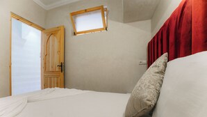 Un dormitorio con cama, una puerta de madera, una ventana pequeña y un cabecero rojo.
