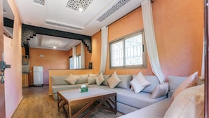 A cozy living room with a sofa, a coffee table, and a kitchen in the background. - Appartement Exceptionnel à Ourika (Marrakech)