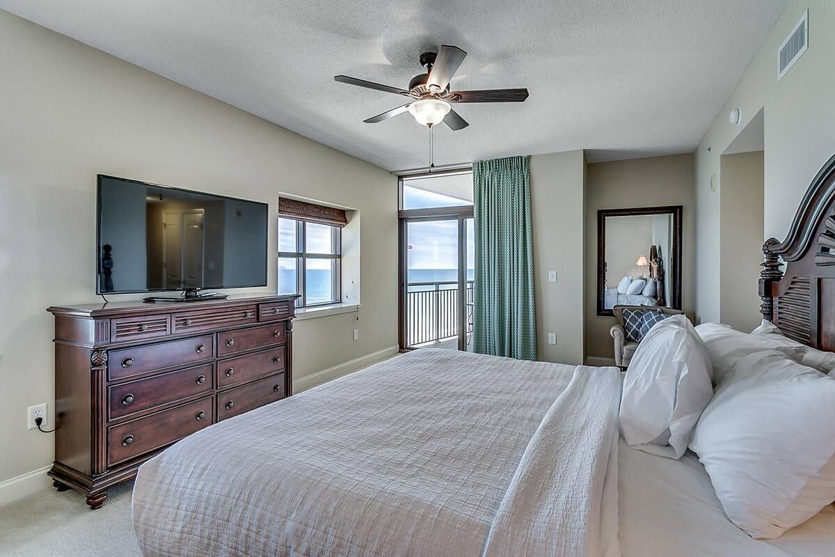 Un dormitorio con cama, cómoda, televisor y balcón con vistas.