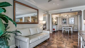 A living room with a white leather sofa, a large mirror, and a dining area with white chairs and a table.