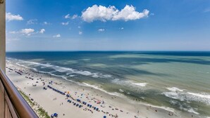 A beach with umbrellas and people, a clear sky, and the ocean.