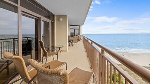 Ein Balkon mit Korbmöbeln, einem Essbereich und Blick auf den Strand.
