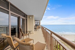 A balcony with wicker furniture, a dining area, and a view of the beach.