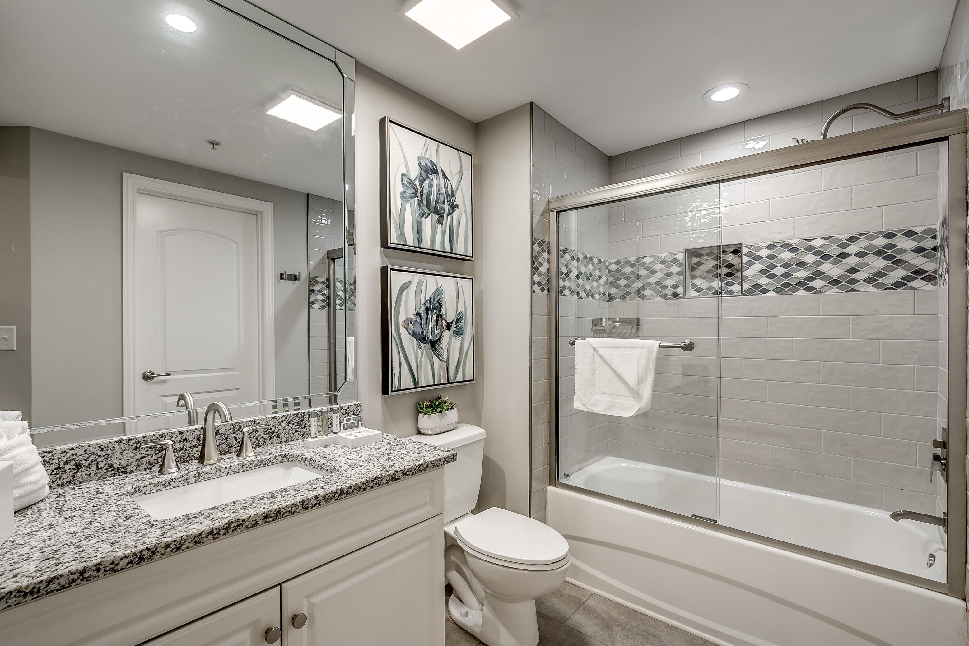 Un baño moderno con lavamanos de granito, inodoro y cabina de ducha con mampara de vidrio.