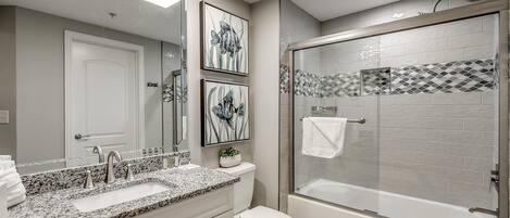 Un baño moderno con lavamanos de granito, inodoro y cabina de ducha con mampara de vidrio.