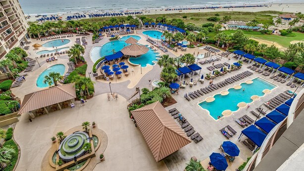 Un resort con varias piscinas, tumbonas y vista a la playa.