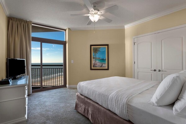 A hotel room with a bed, a TV, a painting, and a balcony with a view.