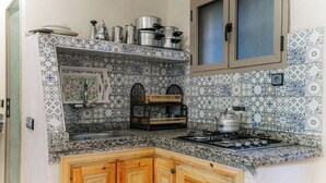 A kitchen with a tiled backsplash, wooden cabinets, a stove, and various kitchen utensils. - Premier Appartement Ourika (Marrakech)