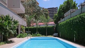 A rectangular swimming pool with a tiled edge, surrounded by a low hedge and a paved walkway. - Nairobi's Oasis: Pool, Gym, & Modern Comforts (Nairobi)