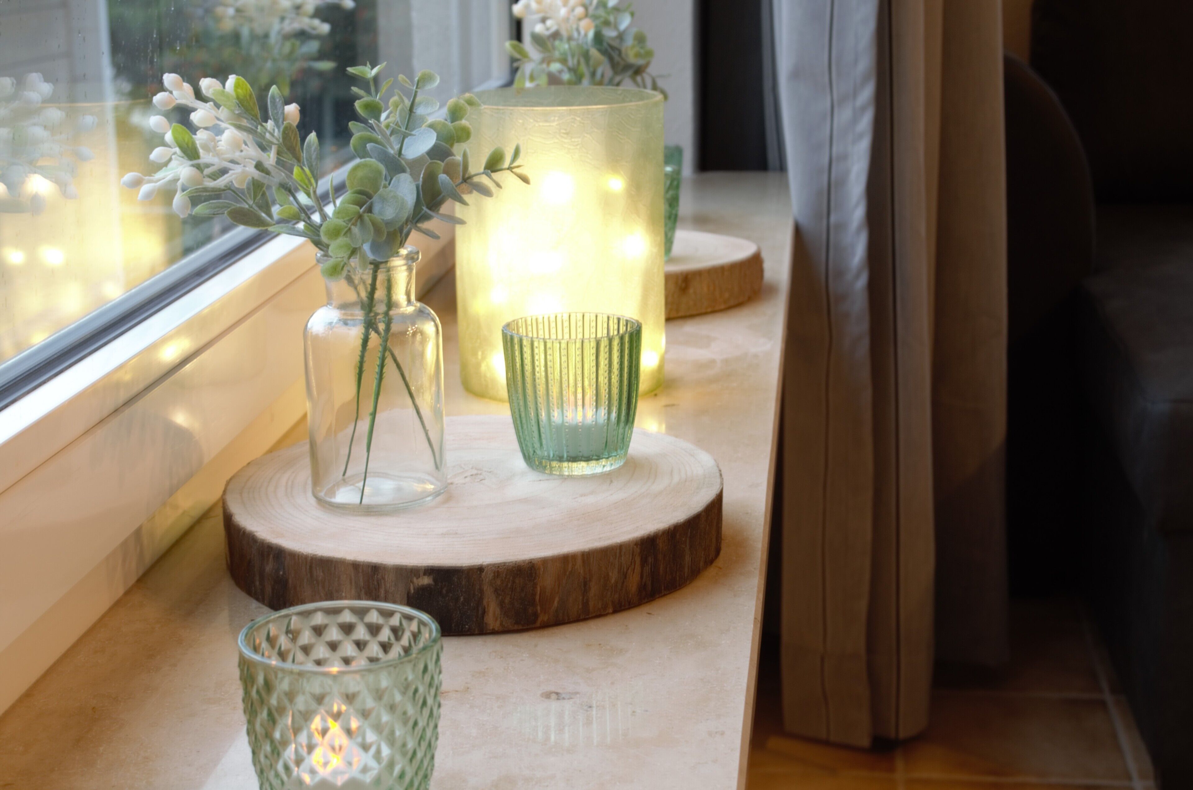 Une table en bois, ornée de porte-bougies en verre et d’un vase contenant des plantes vertes.