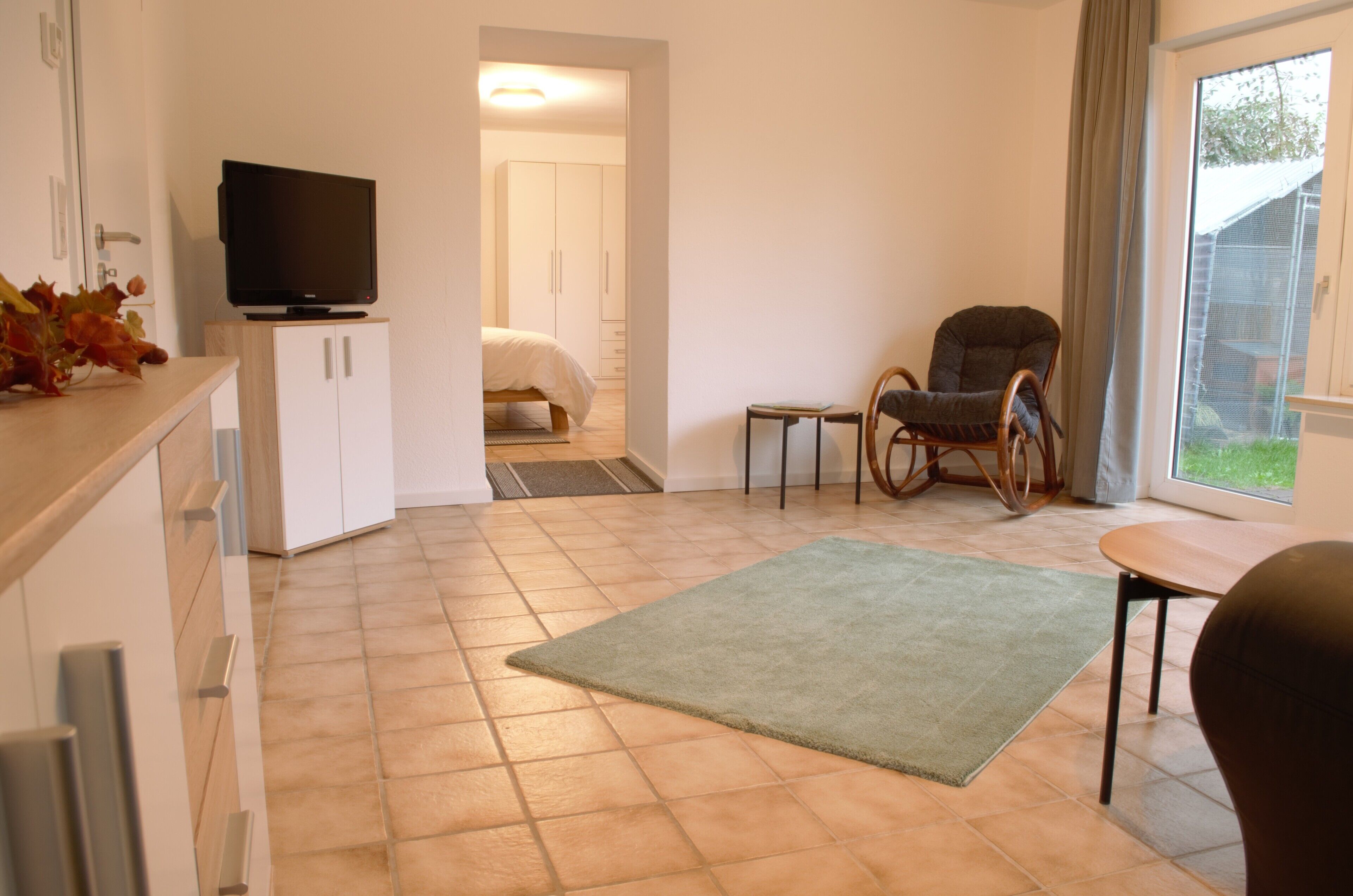 Ein modernes Zimmer mit Fernseher auf einer Kommode, einem Bett, einem Sessel und einem Tisch.