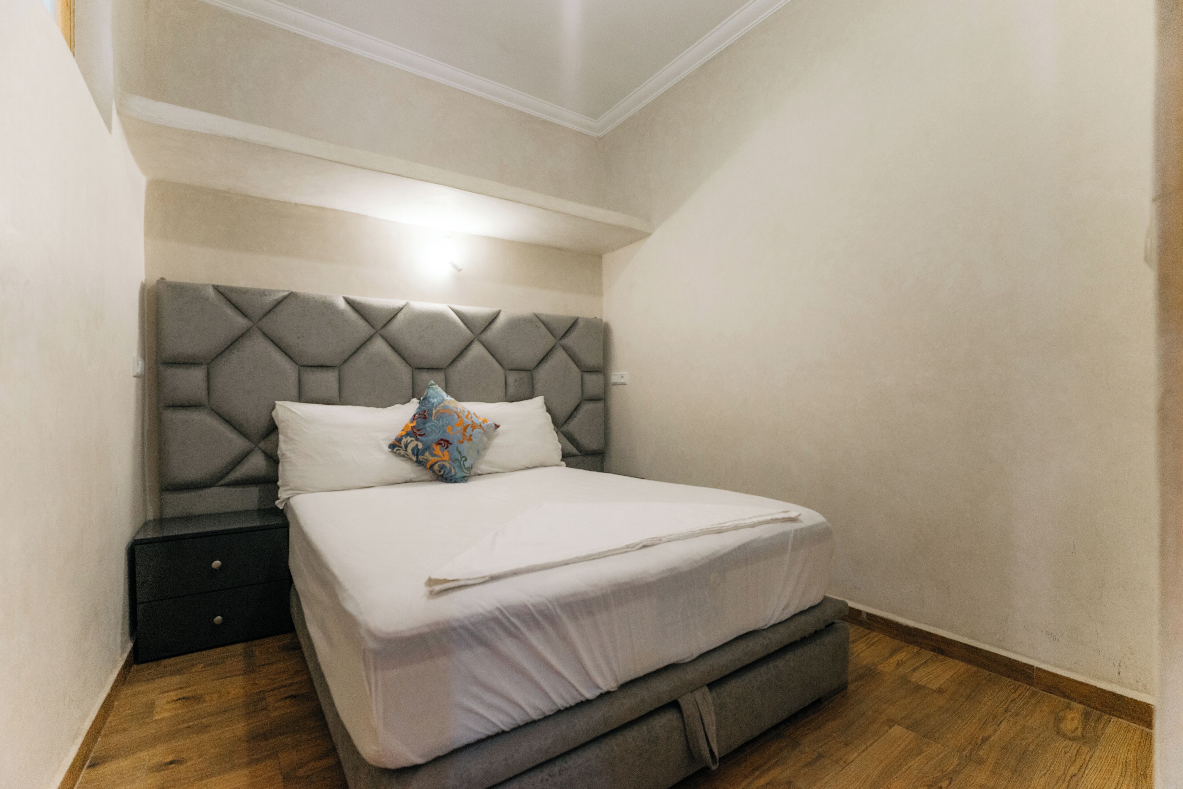 A bedroom with a tufted headboard, a single bed, a nightstand, and a wooden floor.