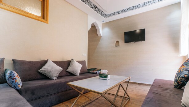Een moderne woonkamer met een bank, een bijzettafeltje en een flatscreen televisie aan de muur.