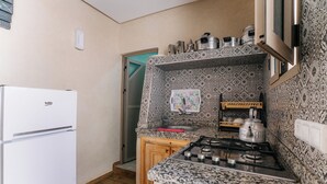 Een keuken met een witte koelkast, een gasfornuis, een betegelde vloer en houten kastjes.