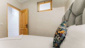 Een slaapkamer met een bed, een houten deur, een klein raam en een decoratief kussen.