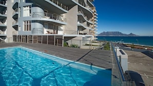 Una piscina con un pontile in legno, un edificio a più piani con balconi e vista sull'oceano.