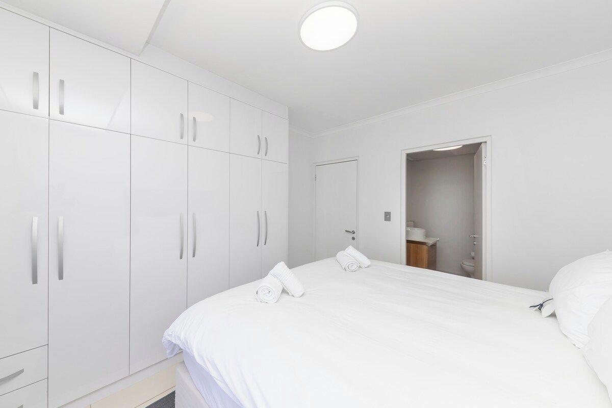 A bedroom with a large bed, white wardrobe, and a door leading to a bathroom.