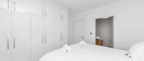 A bedroom with a large bed, white wardrobe, and a door leading to a bathroom.