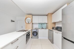 A modern kitchen with white cabinetry, a stainless steel refrigerator, a built-in oven, and a washing machine.