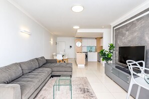 Una sala de estar moderna con un sofá modular, una mesa de centro de vidrio, un televisor de pantalla plana y un comedor con mesa y sillas de vidrio.