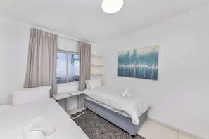 A modern hotel room with two beds, a desk, and a window with curtains.