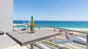 Un balcone con un tavolo, una bottiglia e un bicchiere, vista sulla spiaggia e sull'oceano.
