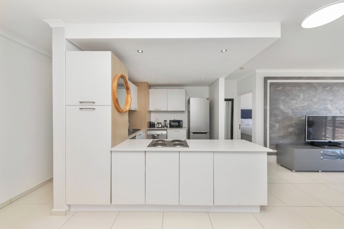 Una cocina moderna con armarios blancos, una isla central con estufa y una luz de aro encima.