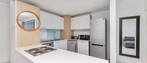 A modern kitchen with white cabinetry, a central island with a stove, and a microwave.