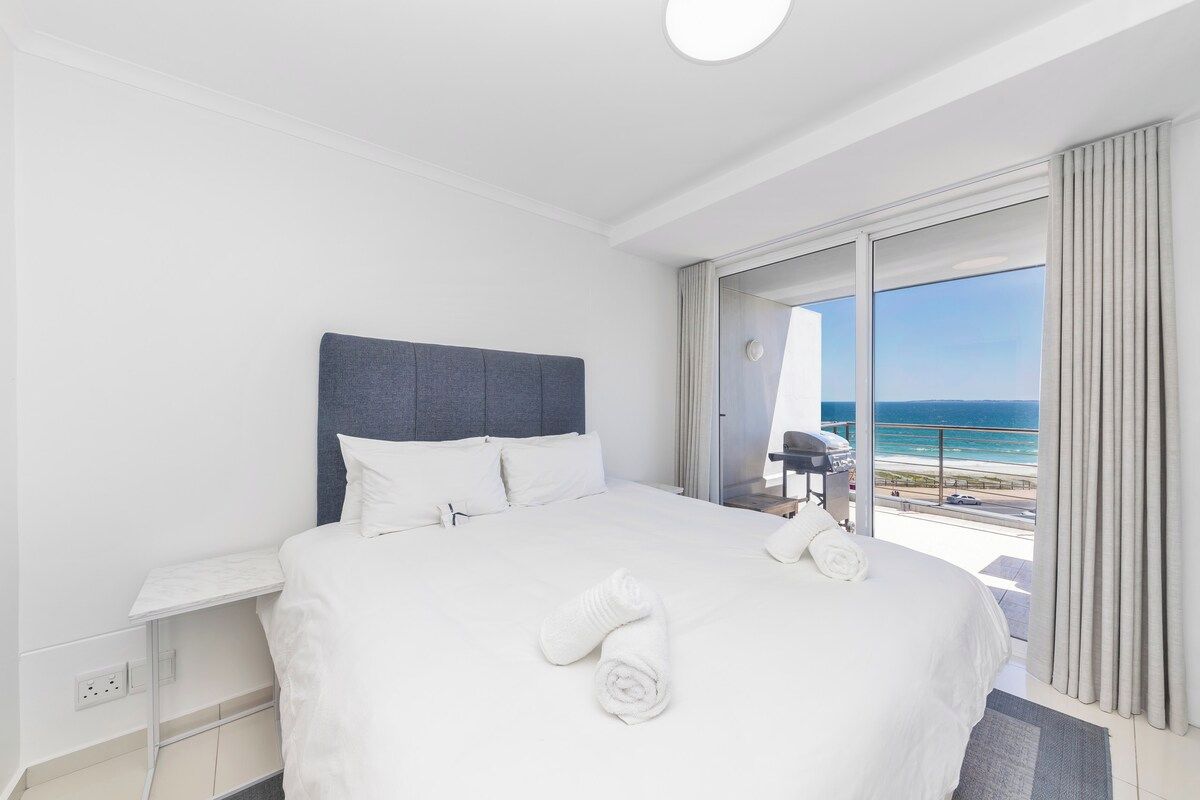 A hotel room with a large bed, a desk, and a view of the ocean.