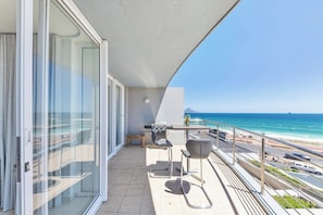 A balcony with a view of the ocean, a grill, and a table with chairs.